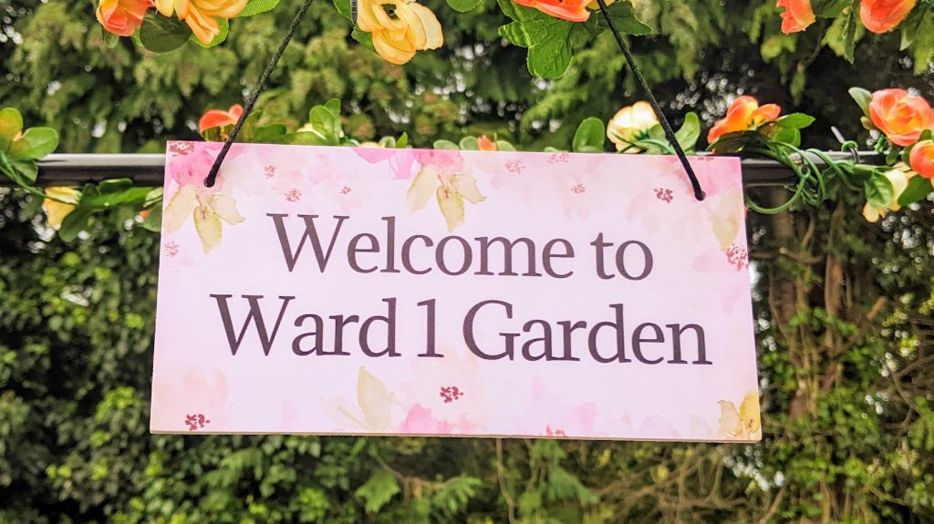 A sign saying "Welcome to Ward 1 Garden" surrounding by flowers.
