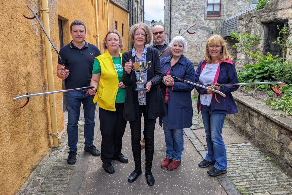 CleanUp group members celebrating outside Bo'ness Library, holding litter pickers.