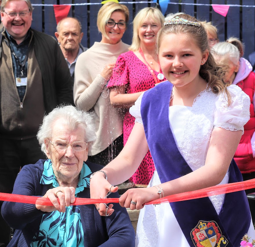 Fair queen and hospital resident, flanked by garden party guests.